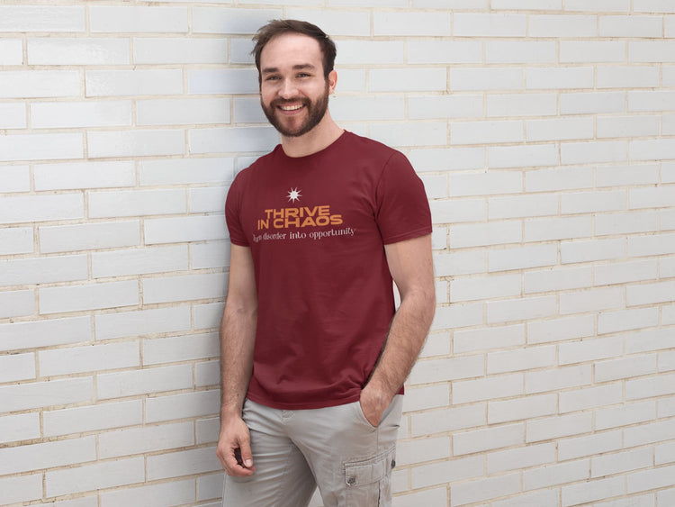 Man wearing a maroon t-shirt with text standing against a light brick wall.
