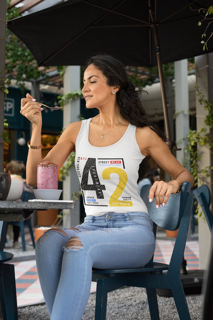 Woman sitting outdoors at a table with a drink, wearing a tank top with a number design.