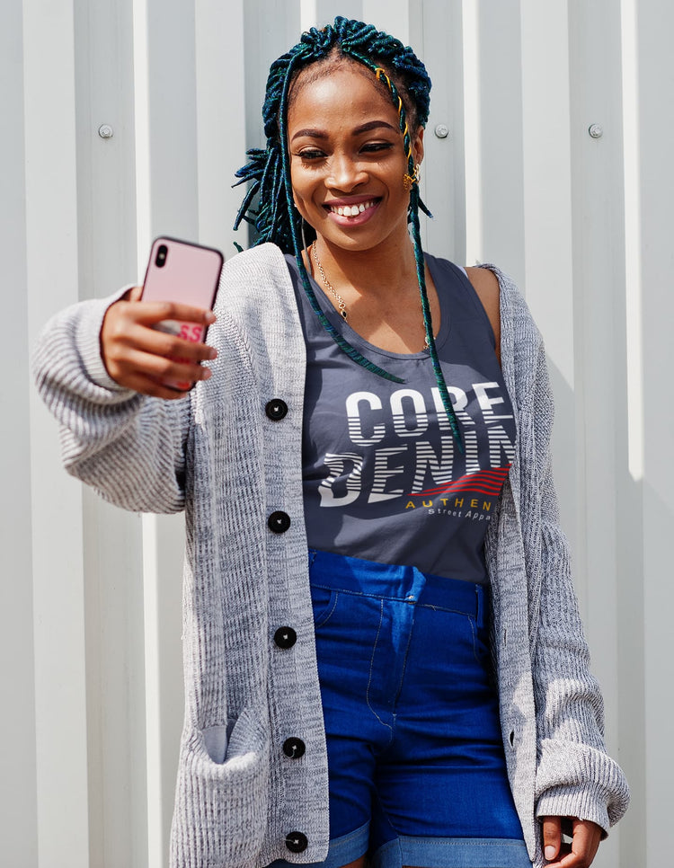 Woman taking a selfie wearing a gray cardigan, gray t-shirt with branding, and blue shorts against a light gray background.