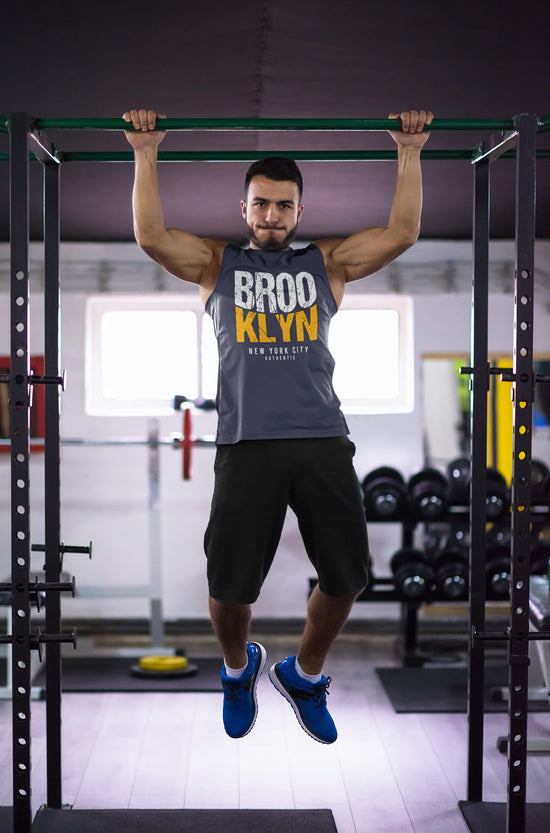Man performing pull-ups in a gym wearing a tank top with &