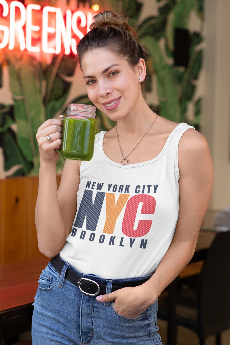 Woman holding a green smoothie in a city-themed tank top with a neon sign in the background.