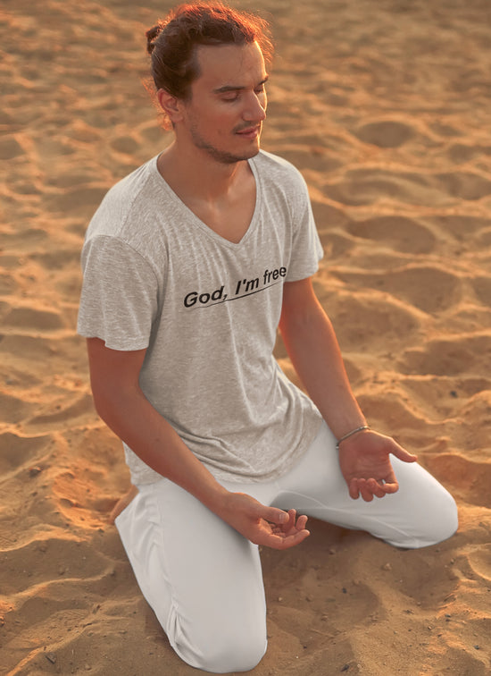 Man kneeling on sand wearing a t-shirt with text, looking contemplative.