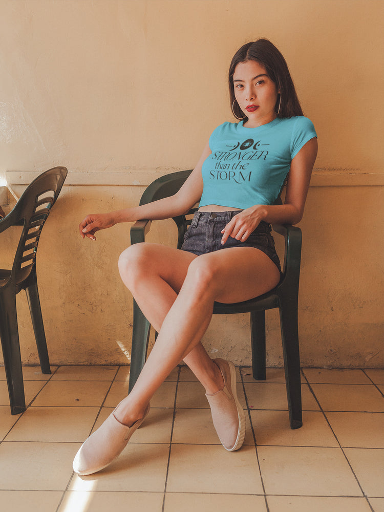 Woman sitting on a chair wearing a blue t-shirt and denim shorts in a tiled room.