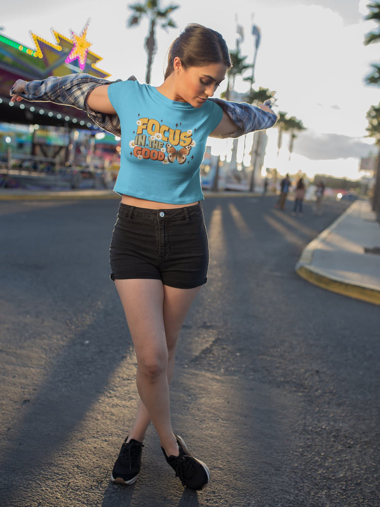 Person wearing a blue crop top with text and black shorts at an outdoor setting.