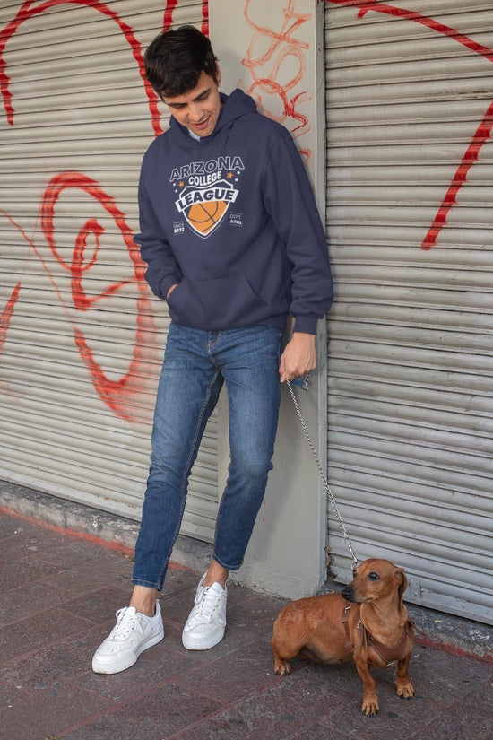 Person wearing a hoodie and jeans standing next to a dog on a street with graffiti.