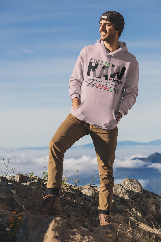 Person wearing a pink hoodie with text and brown pants standing on a mountain with a blue sky and clouds in the background.