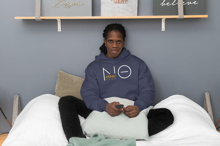 Person sitting on a bed wearing a hoodie with a logo, holding a phone, against a gray wall with shelves displaying motivational word pillows.