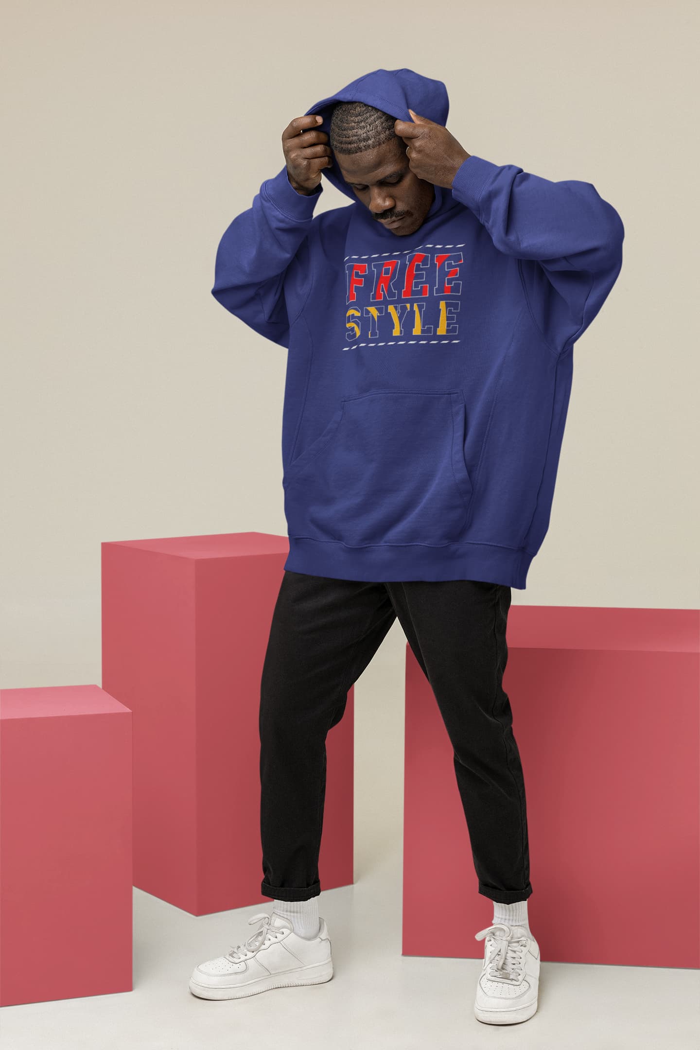 Person wearing a blue hoodie with text, standing on pink blocks against a beige background