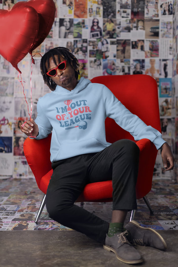 Person sitting on a red chair holding heart-shaped balloons, wearing a light blue hoodie with text and dark pants.
