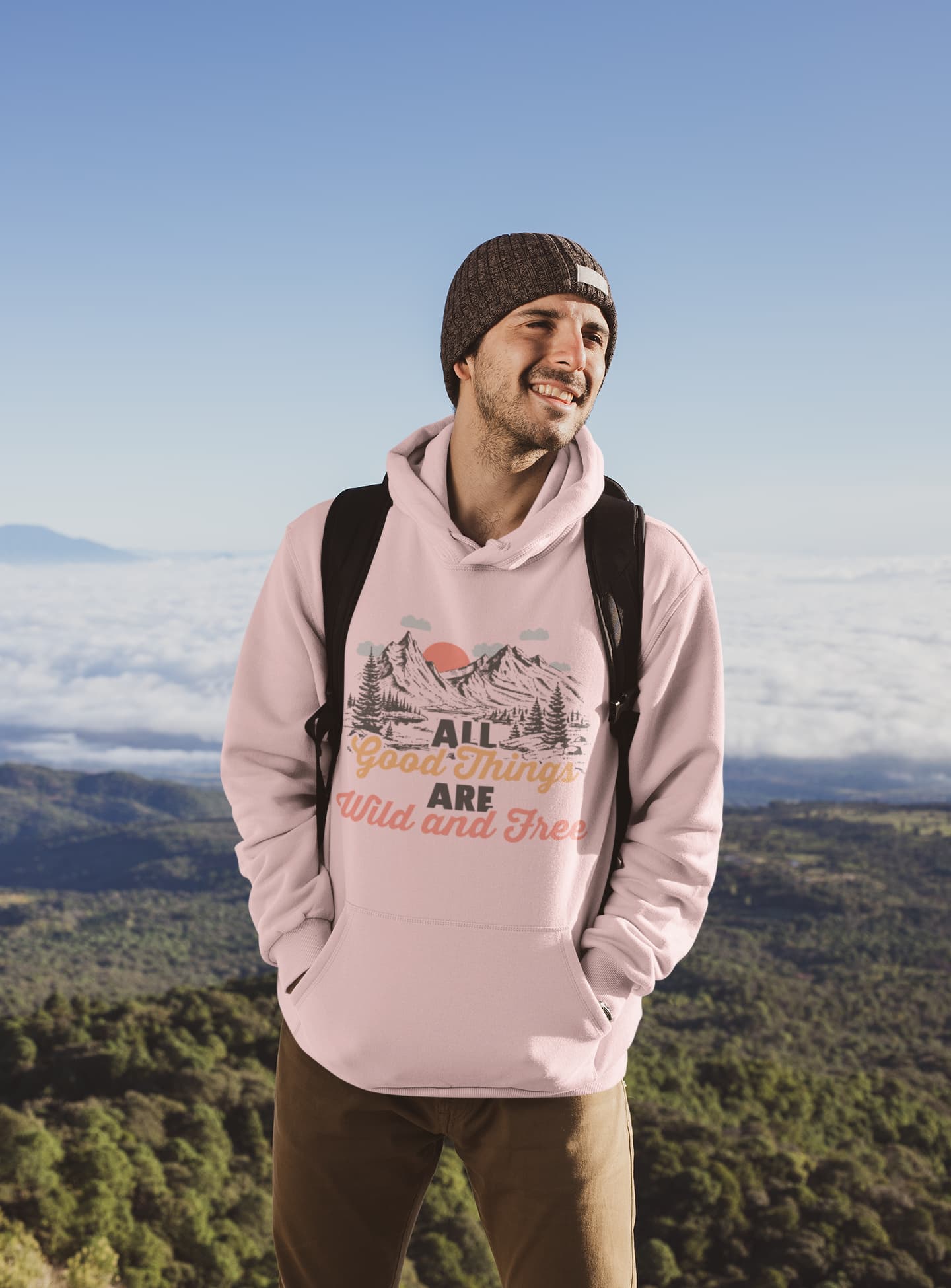 Man wearing a pink hoodie with a nature graphic and text, standing in a scenic outdoor setting.