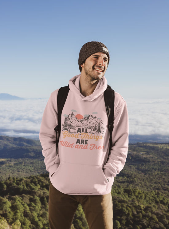 Man wearing a pink hoodie with a nature graphic and text, standing in a scenic outdoor setting.