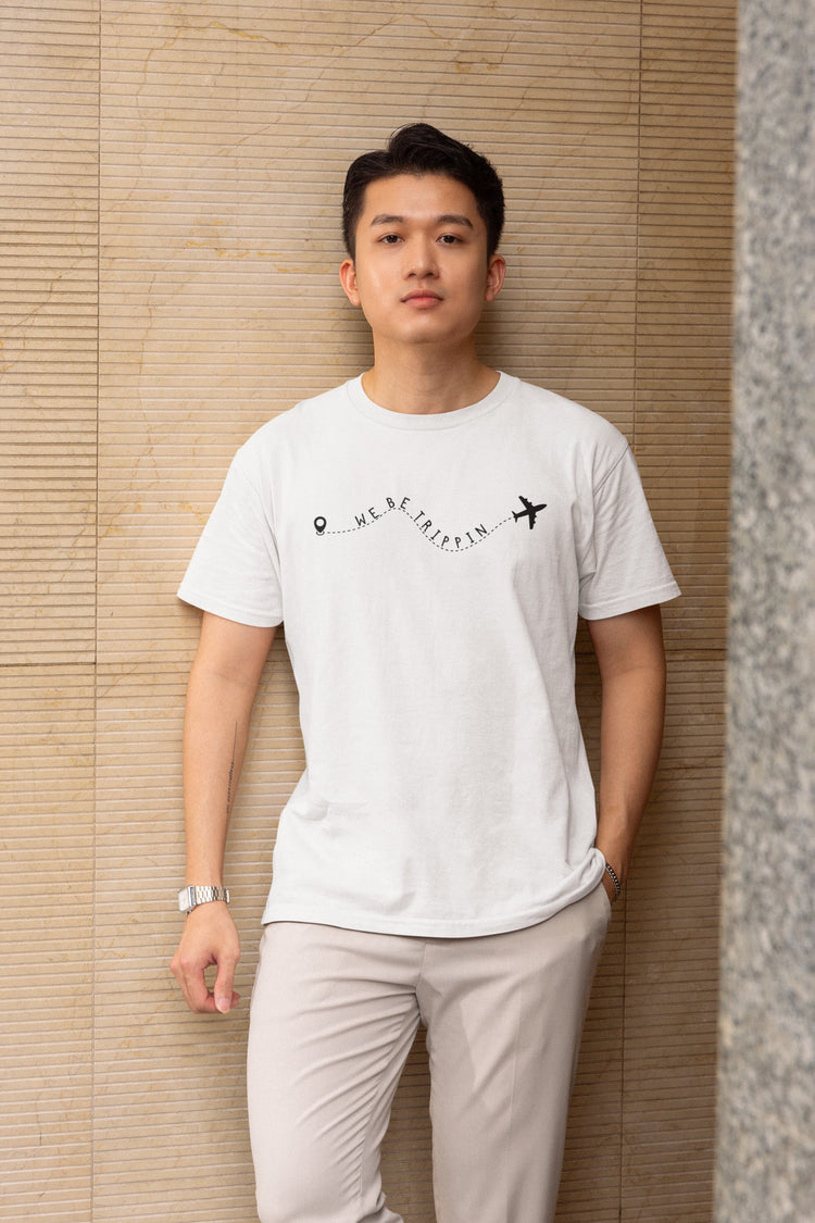 Man wearing a white t-shirt with text and graphics against a beige wall.