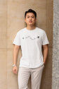Man wearing a white t-shirt with text and graphics against a beige wall.