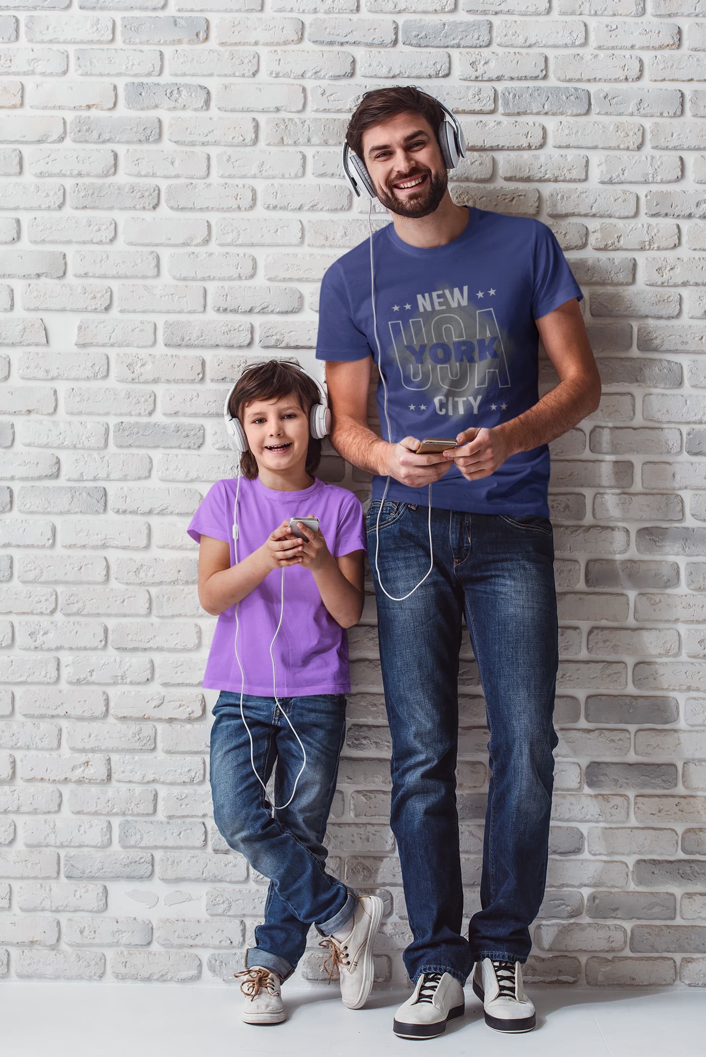 Man and child standing against a white brick wall, both wearing headphones.