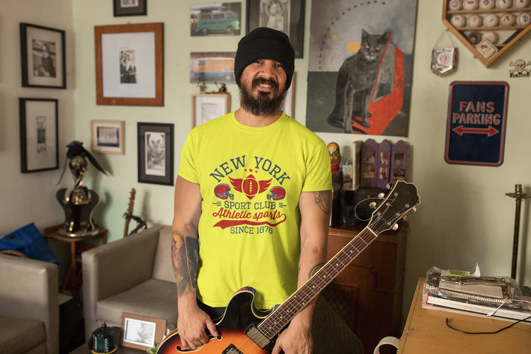 Person wearing a bright yellow t-shirt with text, holding a guitar in a room with various decorations.