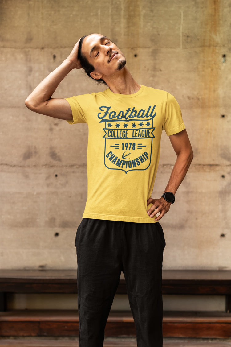 Man wearing a yellow t-shirt with text, standing against a concrete wall.