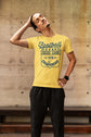 Man wearing a yellow t-shirt with text, standing against a concrete wall.