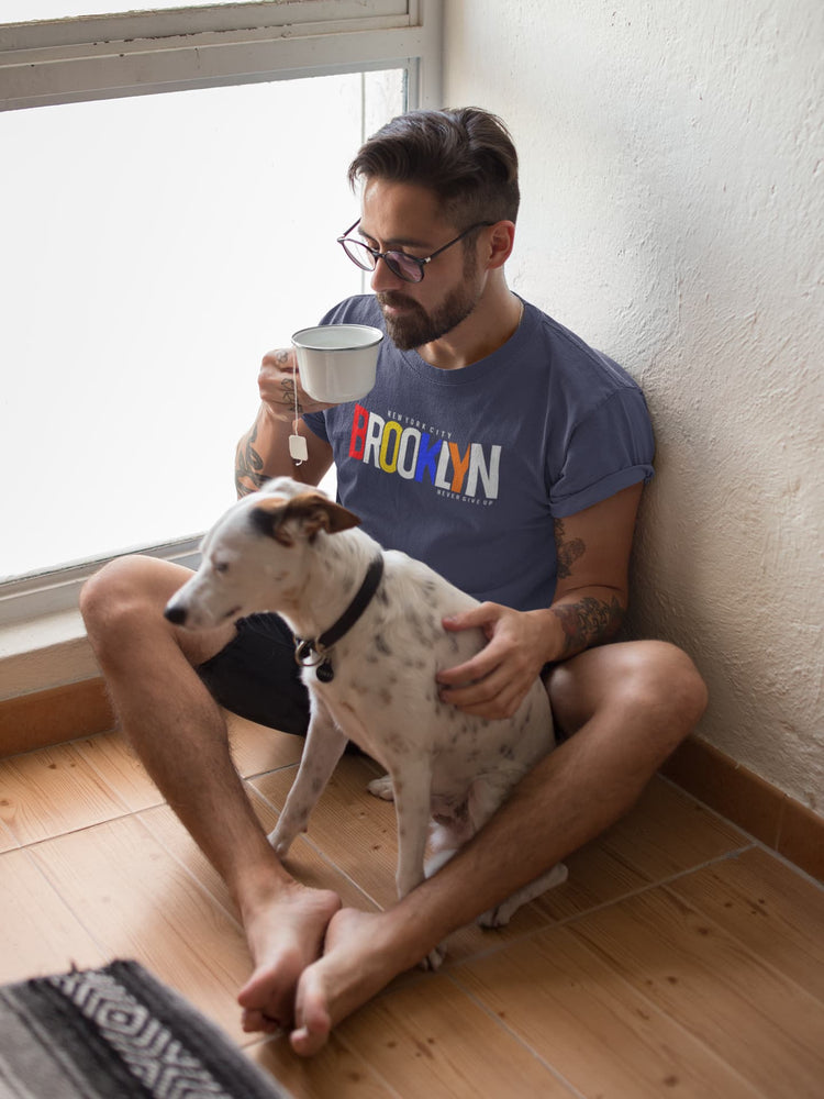 Man sitting on the floor with a dog, holding a mug, wearing a &