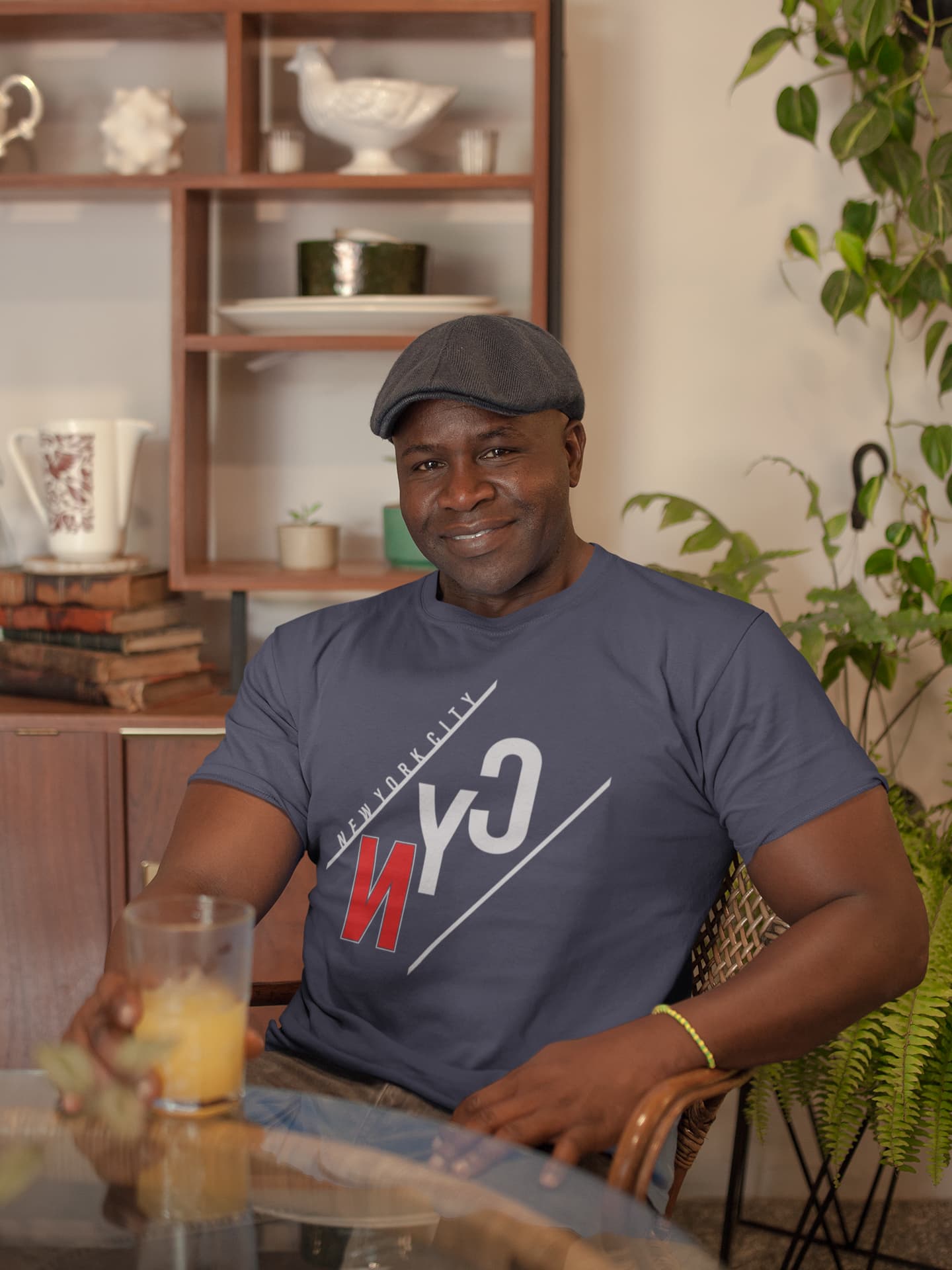 Man wearing a blue t-shirt with a logo, holding a glass of orange juice in a casual setting.