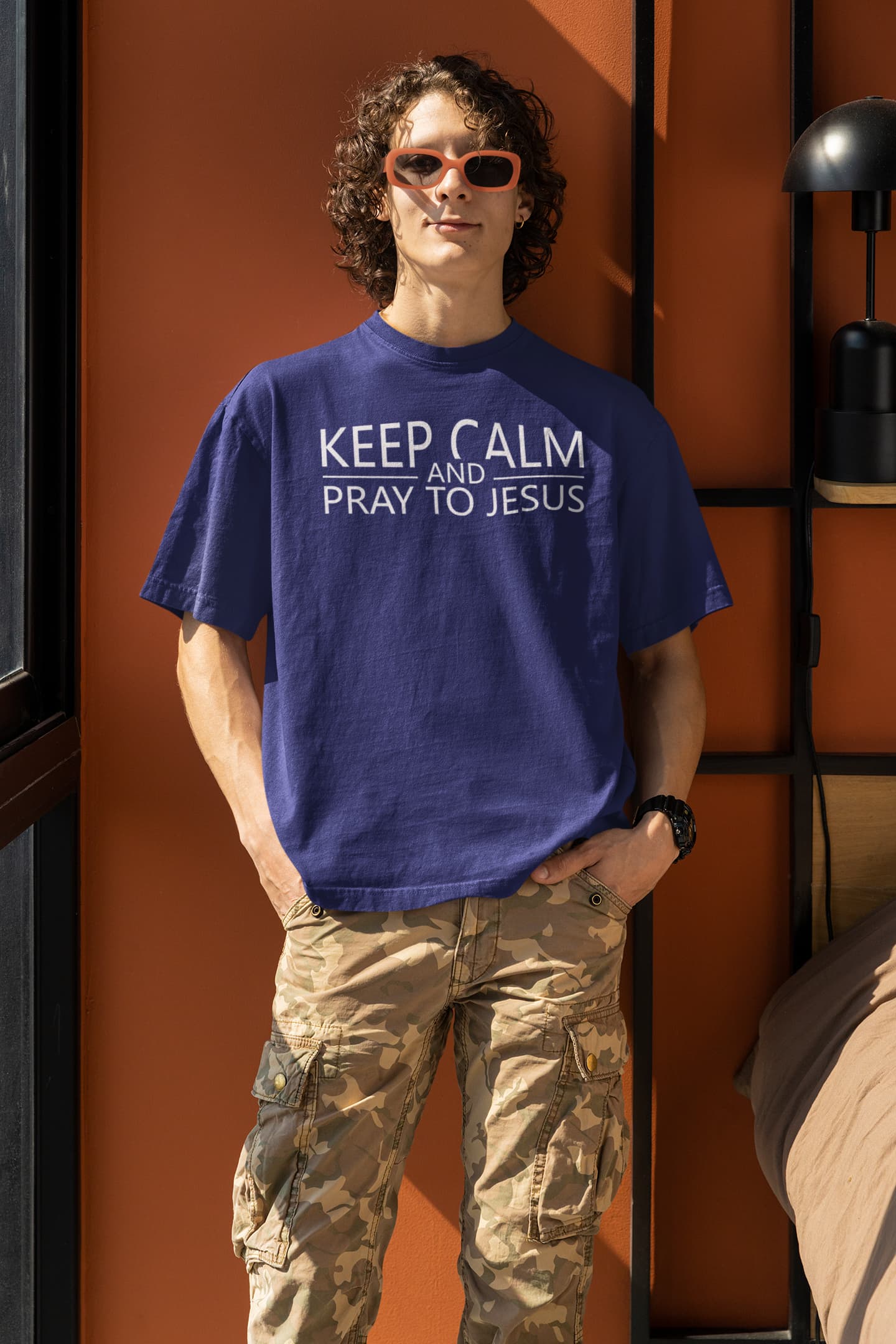 Person wearing a blue t-shirt with text, standing against an orange wall.