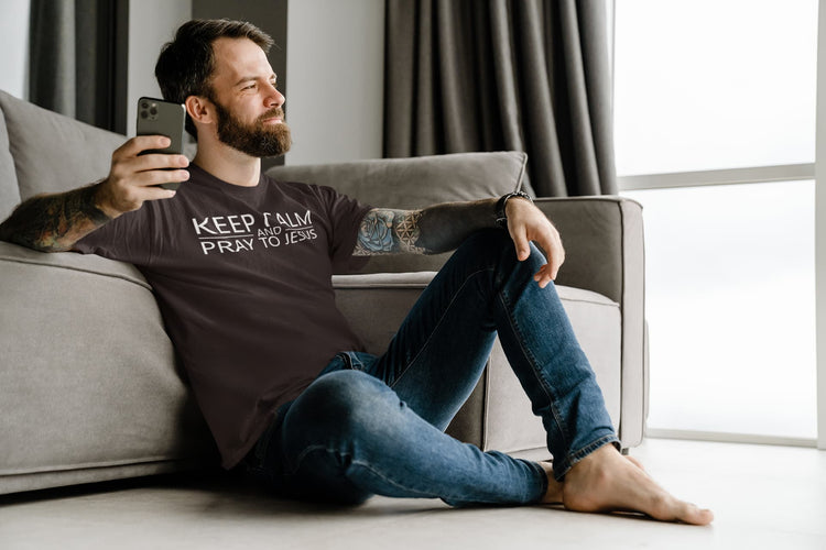 Man sitting on a couch wearing a t-shirt with text, holding a phone.