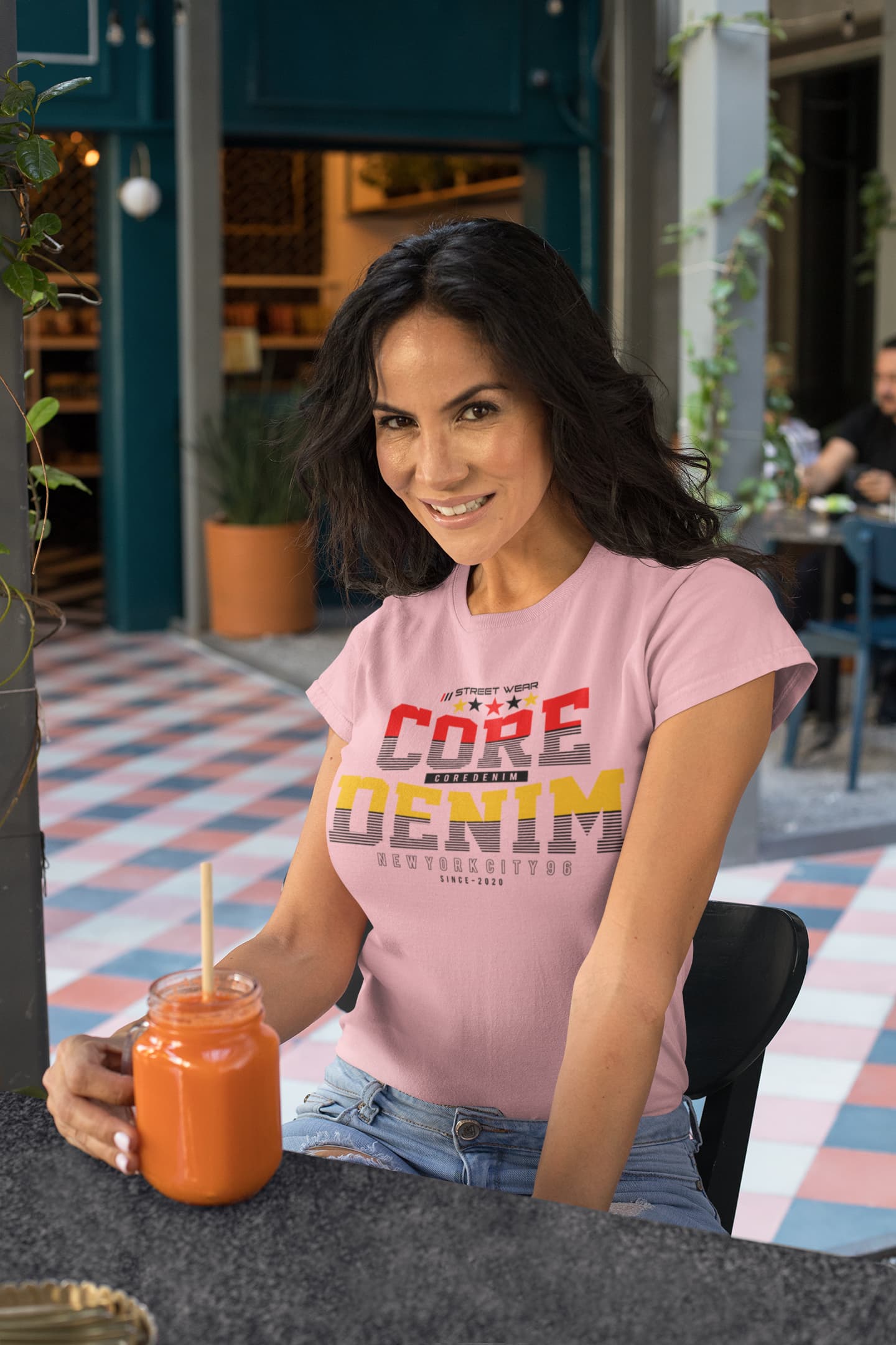 Woman in pink t-shirt with colorful text sitting outdoors holding a smoothie.