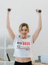 Woman exercising with dumbbells wearing a sleeveless shirt with text in a home setting