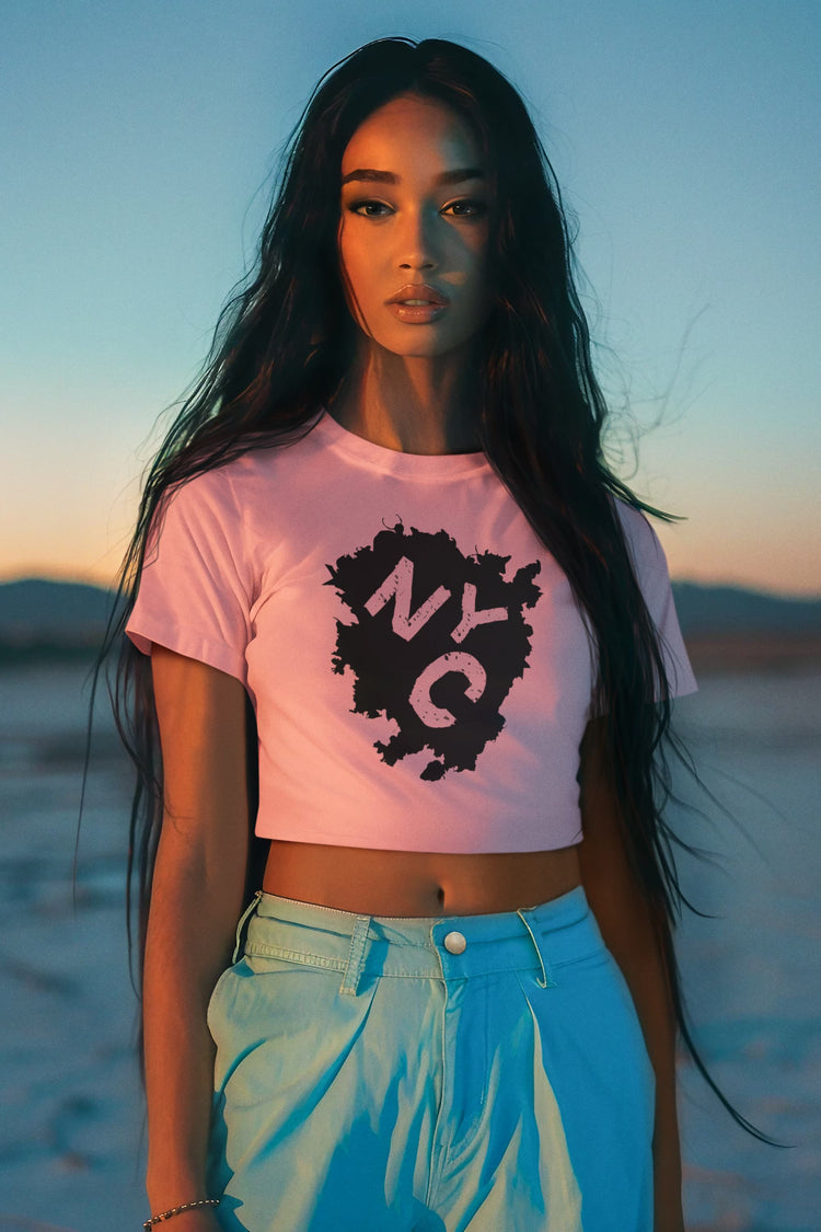 Woman wearing a pink t-shirt with a logo and light blue jeans standing on a beach at sunset.