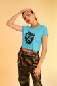 Woman wearing a blue crop top with a black design and camouflage pants on a beige background