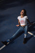 Woman sitting on a blue basketball court wearing a white t-shirt and jeans.