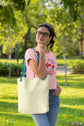 Woman holding a beige tote bag outdoors in a park