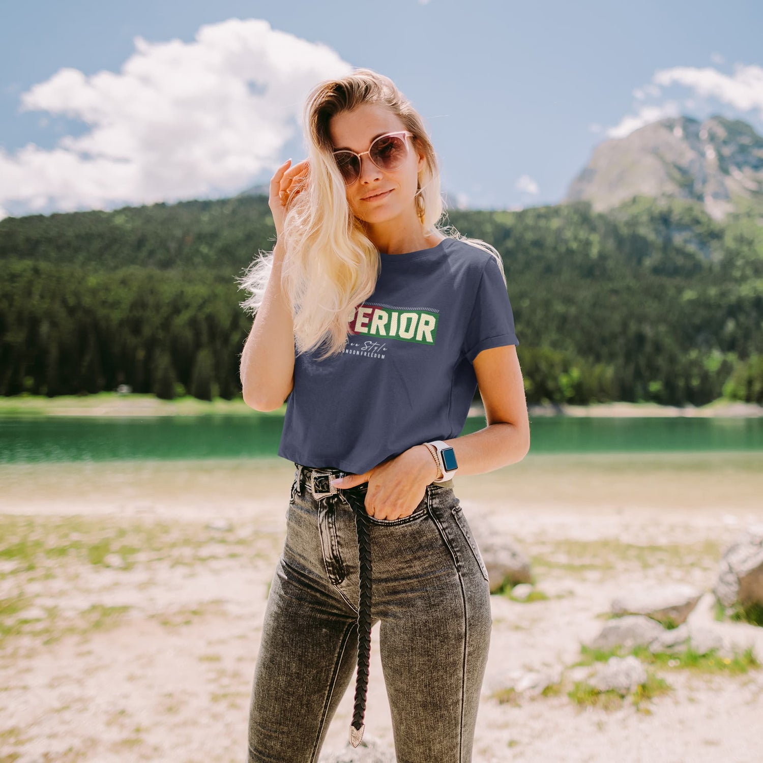Woman wearing a t-shirt with text standing in a scenic outdoor setting with mountains and a lake.