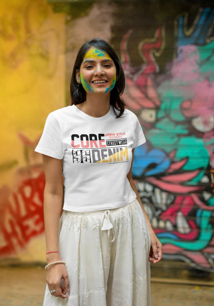 Woman wearing a white t-shirt with colorful graphics in front of a graffiti wall.