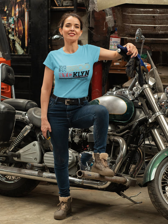 Woman in a blue t-shirt standing next to a motorcycle in a garage.