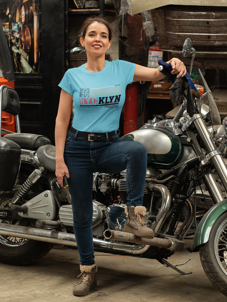 Woman in a blue t-shirt standing next to a motorcycle in a garage.