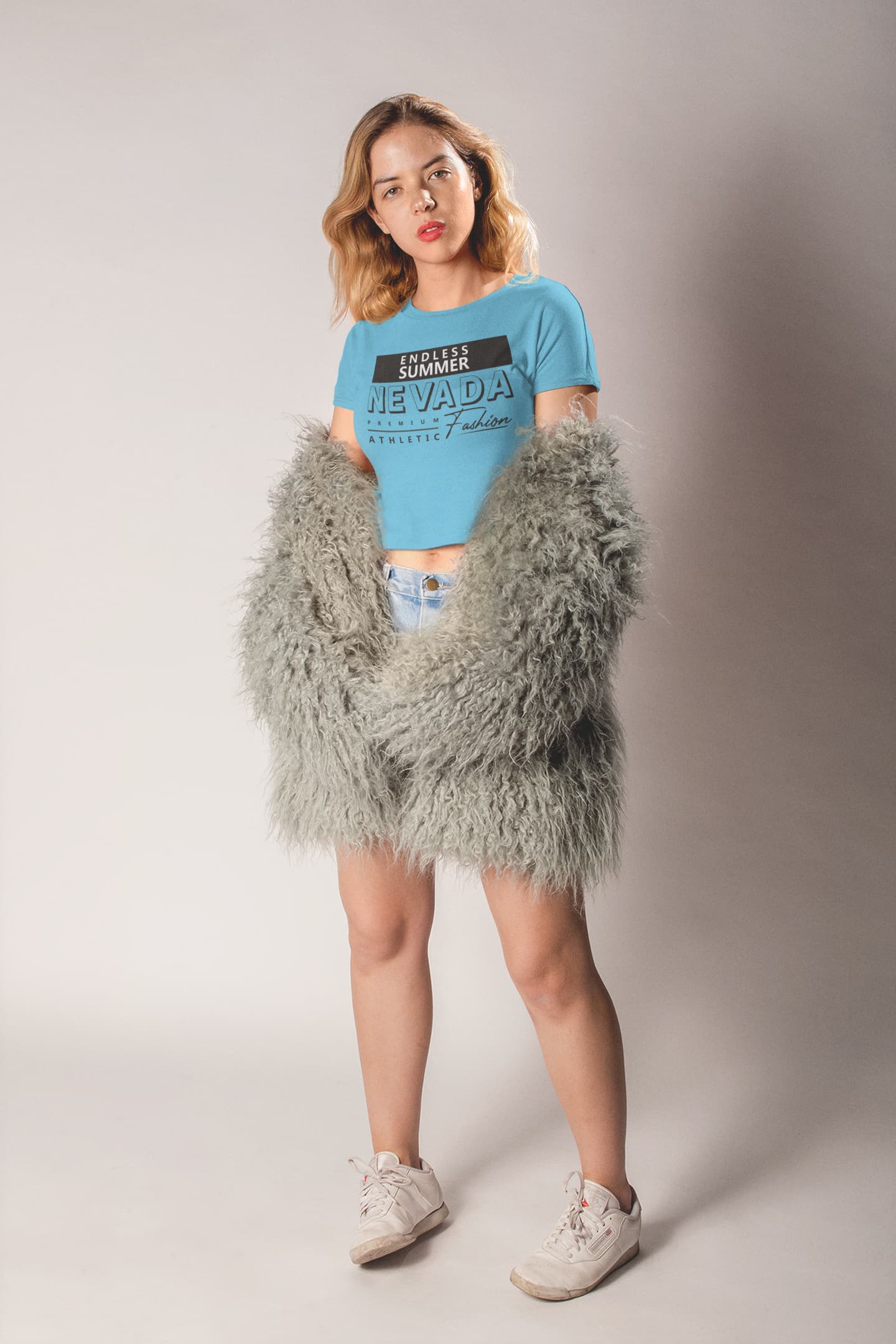 Woman wearing a blue t-shirt and gray fluffy coat against a plain background