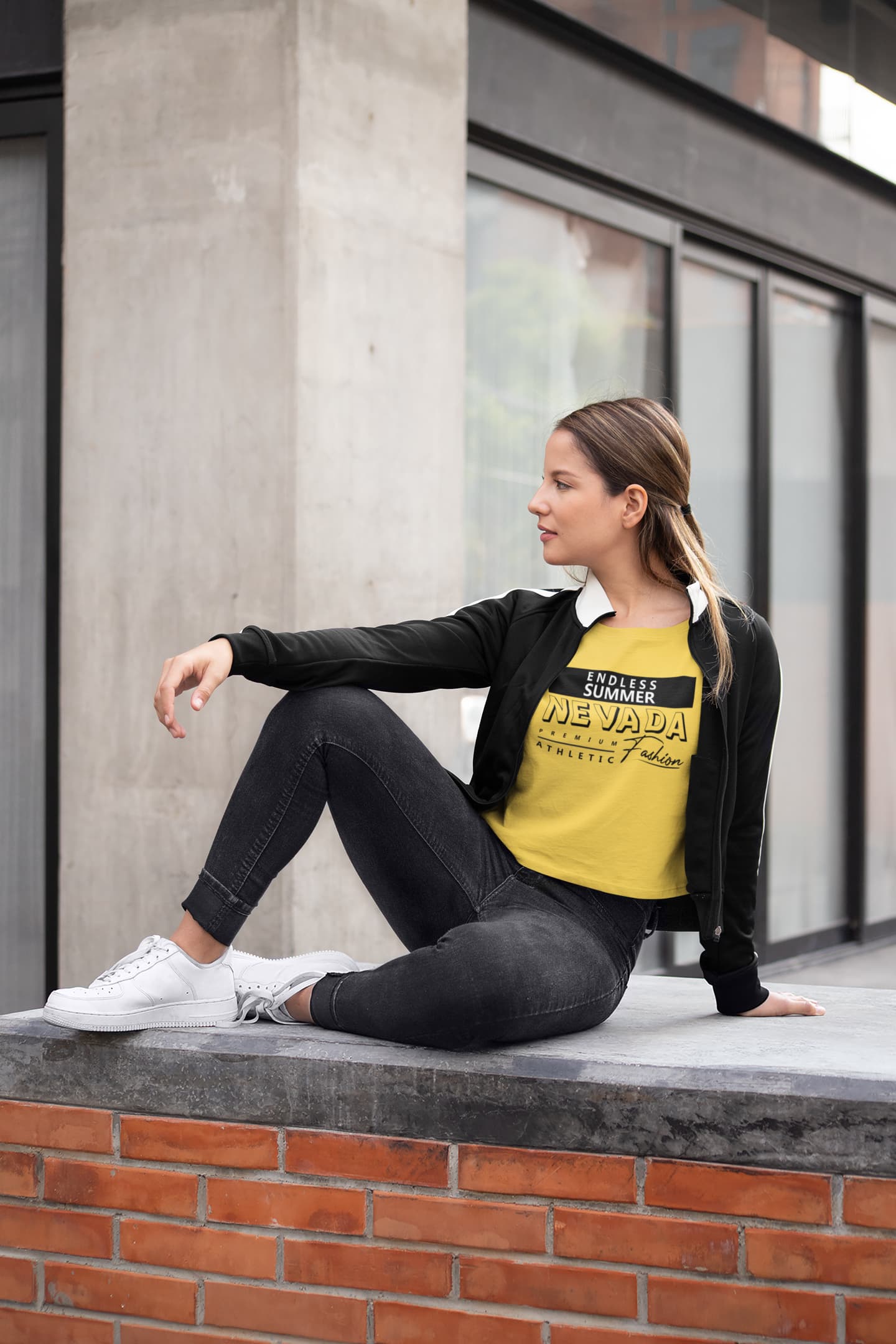 Woman sitting on a ledge wearing a yellow t-shirt with text and black jacket.