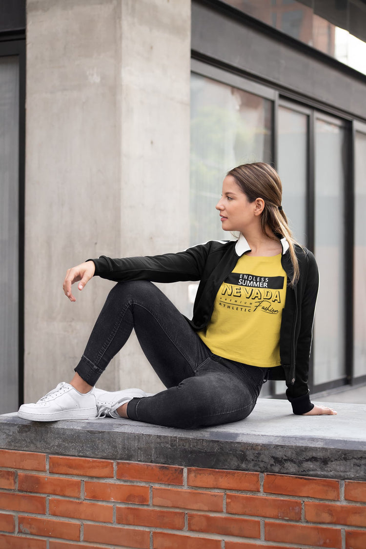 Woman sitting on a ledge wearing a yellow t-shirt with text and black jacket.