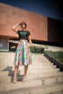 Woman standing on steps wearing a colorful skirt and black top with text.