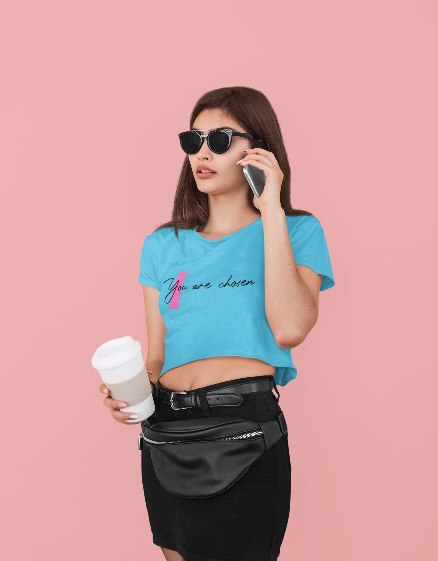Woman wearing a blue t-shirt with text, holding a phone and coffee cup on a pink background
