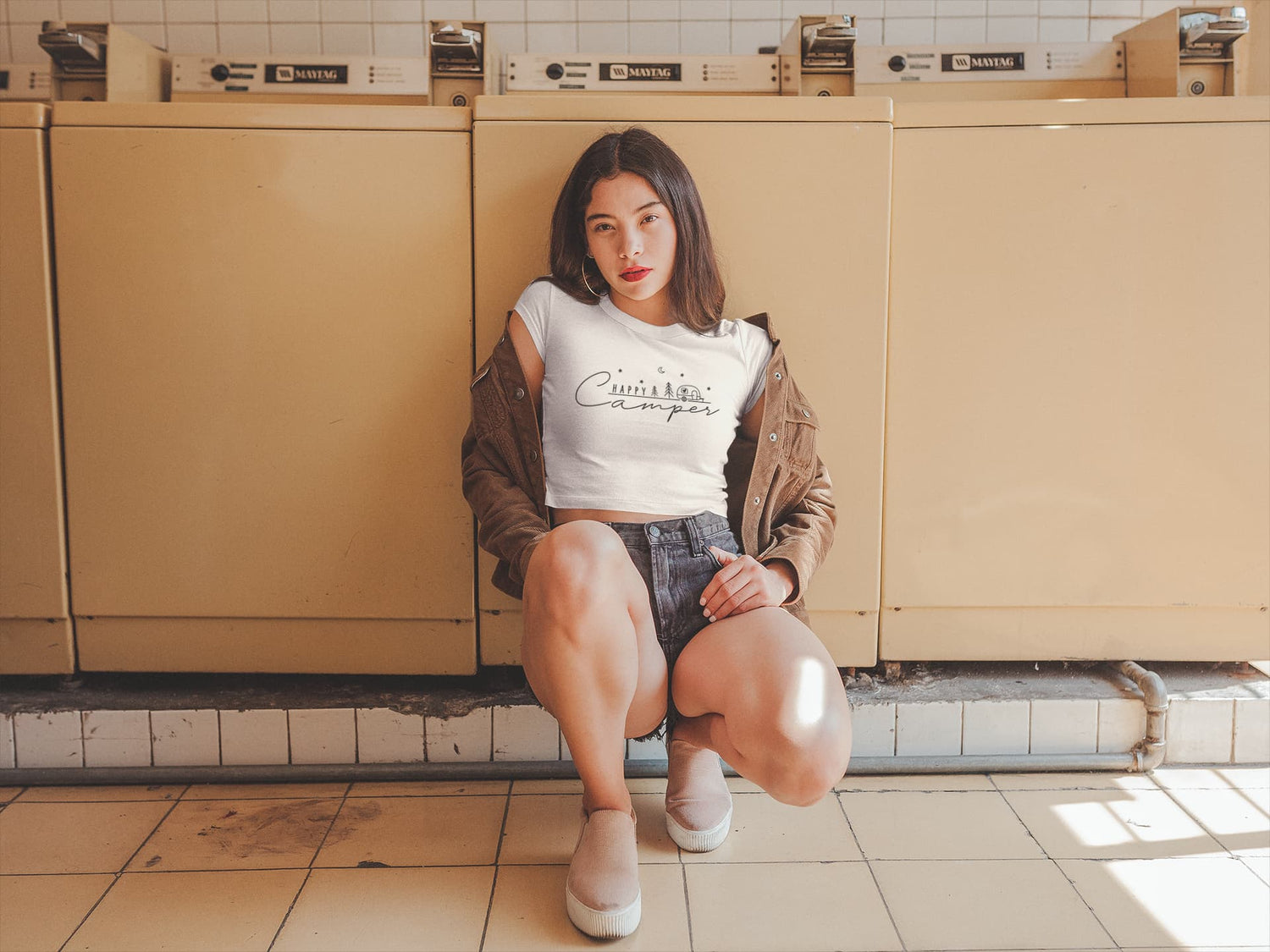 Woman sitting on a tiled floor in a public restroom with beige stalls.