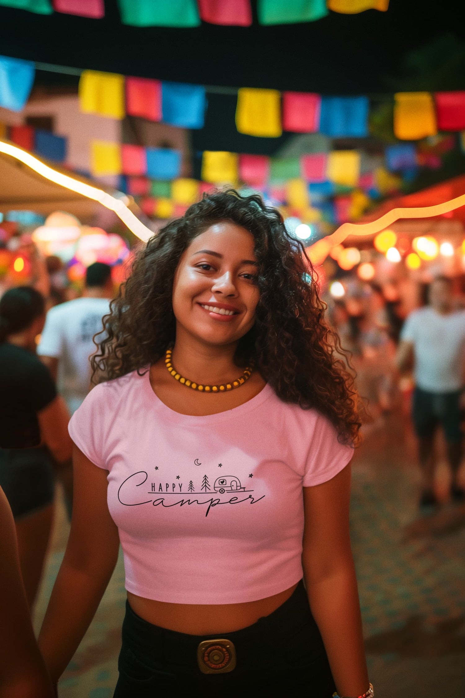 Woman in a pink t-shirt with a logo at a festive outdoor event with colorful flags and lights.