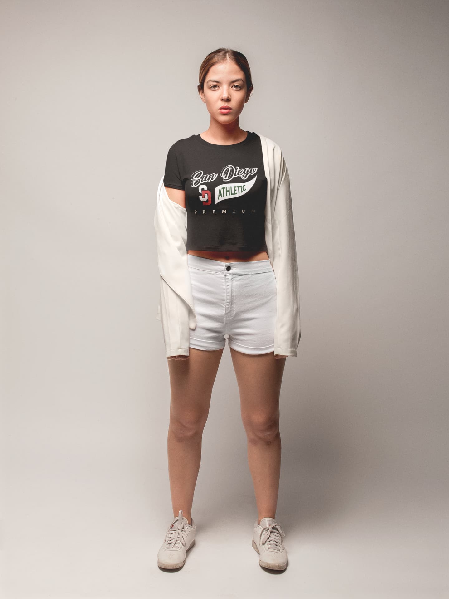 Person wearing a black crop top with visible branding, white shorts, and a beige cardigan on a plain background