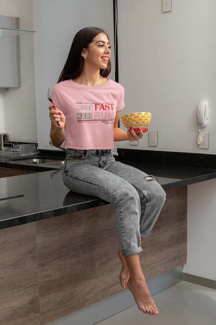 Woman sitting on a kitchen counter holding a bowl of fruit, wearing a pink t-shirt with text.