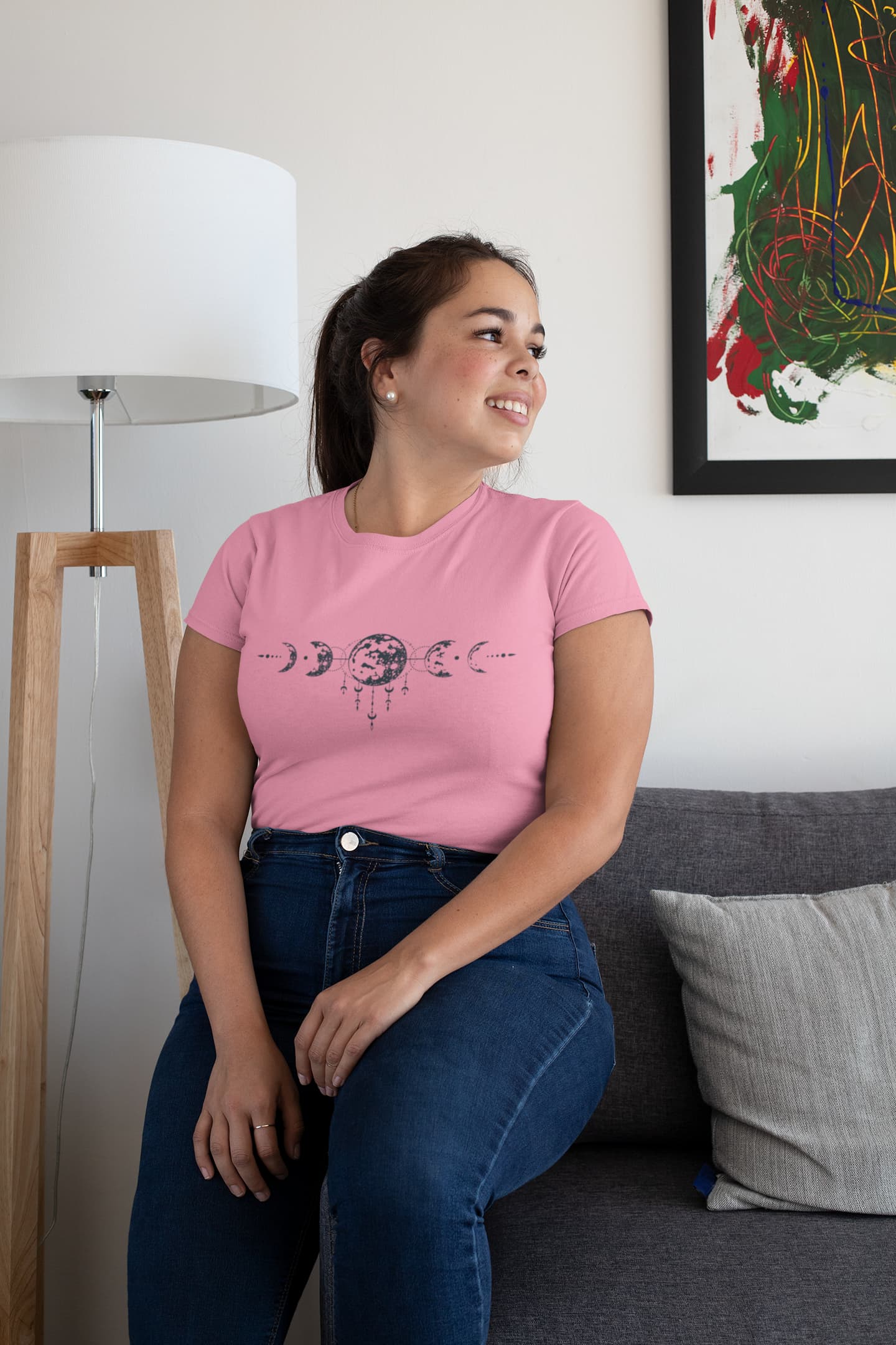 Woman wearing a pink t-shirt with a graphic design, sitting on a couch in a living room.