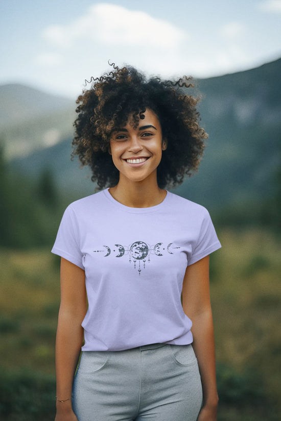 Person wearing a light purple t-shirt with a graphic design, standing outdoors with mountains in the background
