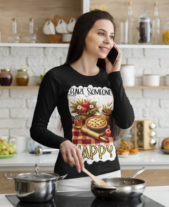 Woman in a kitchen wearing a black long-sleeve shirt with a pie design and text.