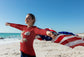 Person holding an American flag on a beach with a clear blue sky