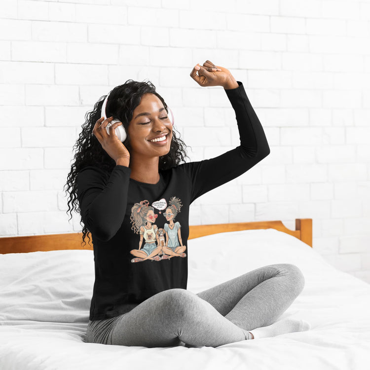 Woman wearing a black long-sleeve shirt with a graphic design, sitting on a bed.