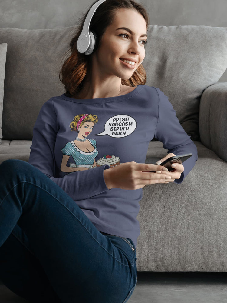 Woman sitting on a couch wearing a purple sweatshirt with graphic designs, using a phone.